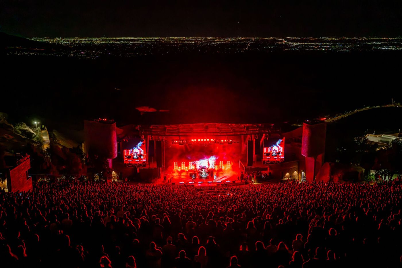Alkaline Trio playing an outdoor amphitheatre at night, stage lit red with city lights behind