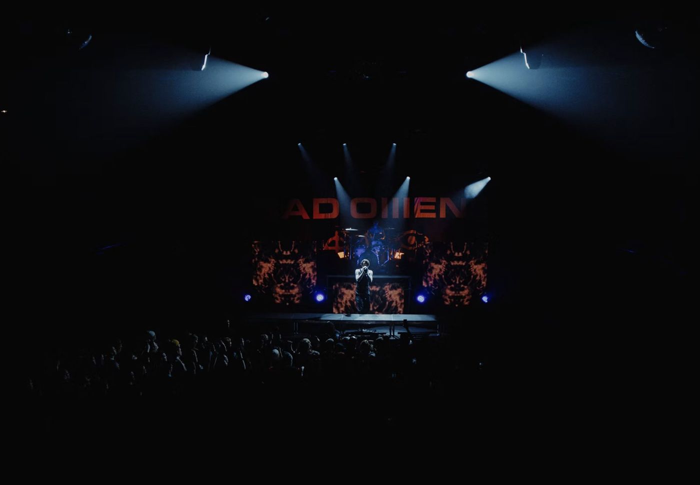 Bad Omens singer alone on a riser, white beams cutting through the dark above flame-pattern video panels
