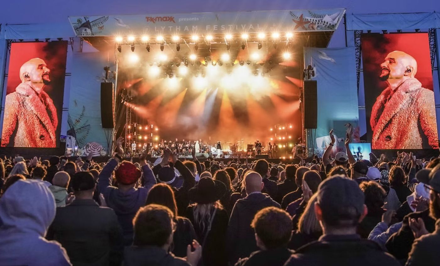 James on a festival main stage, warm beams through haze and the singer on the side screens