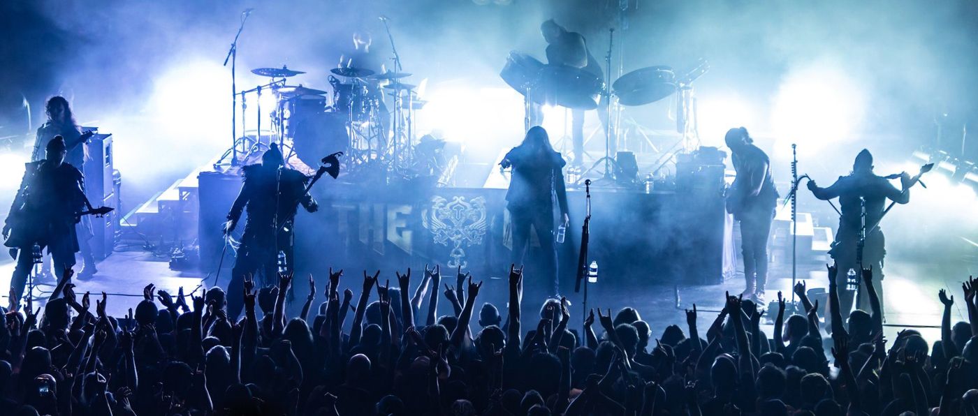 The HU silhouetted in blue haze with white backlight, the crowd’s raised hands in the foreground